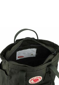 Interior de una mochila Fjällräven Kanken verde oscuro con un compartimento con cremallera, correas de tela ajustables y una etiqueta con nombre visible.