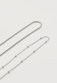 Δύο αλυσίδες από ασημί μέταλλο πάνω σε λευκή επιφάνεια, η μία με μικρές λείες χάντρες και μεγαλύτερες χάντρες ανάμεσά τους, η άλλη με λεπτή, σφικτά συνδεδεμένη υφή.