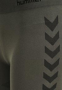 Donkergroene legging met een gestructureerde, elastische tailleband. Aan de zijkant bevindt zich een zwart chevronpatroon voor extra detail en ontwerp.