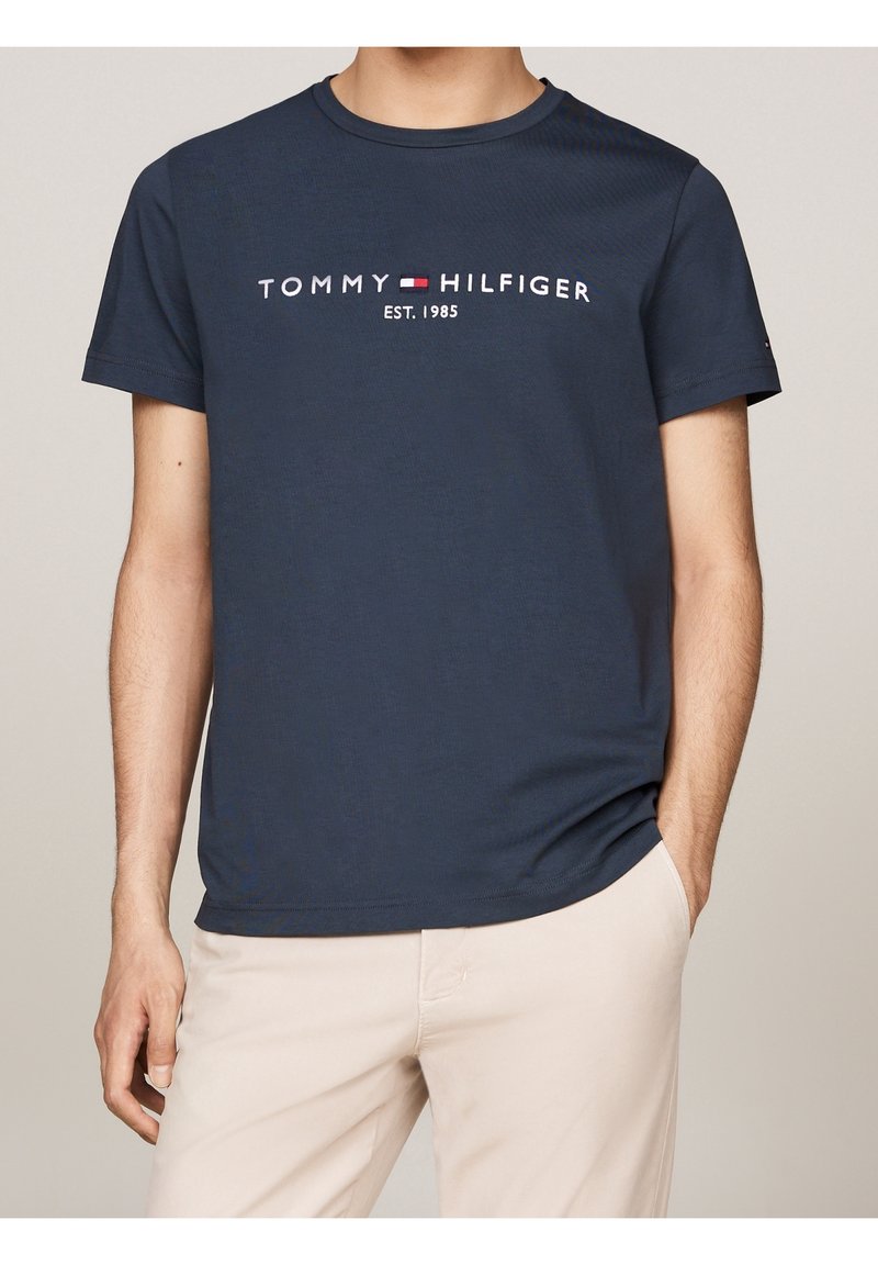 Granatowa bawełniana koszulka z krótkim rękawem, okrągłym dekoltem, z logo "TOMMY HILFIGER EST. 1985" w białych i czerwonych grafikach na przodzie.