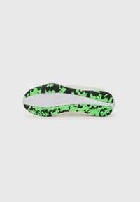 Semelle de chaussure avec un design texturé noir et un motif vert vif, présentant une semelle intermédiaire blanche et un profil géométrique pour l'adhérence.