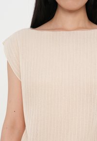Beige ribbed top with a wide boat neckline and short sleeves. The fabric appears soft with a subtle texture.