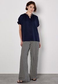 Blusa navy a maniche corte con scollatura a V, abbinata a pantaloni a vita alta con gambe larghe a righe bianche e nere. Include sandali flat.
