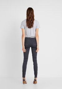 Camiseta gris, jeans oscuros ajustados y sandalias de tacón negro. Los jeans tienen un ligero estiramiento y un diseño estándar de bolsillo trasero.