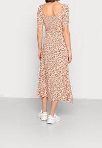 Robe midi florale avec de courtes manches bouffantes, un buste froncé et un fond rose orné de fleurs multicolores. Portée avec des baskets blanches.