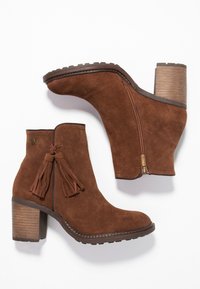 Brązowe zamszowe botki za kostkę z teksturowanym drewnianym obcasem, bocznym zamkiem błyskawicznym i dekoracyjną frędzelkową detalem. Projekt charakteryzuje się zaokrąglonym kształtem palców.