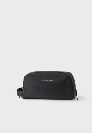 Trousse de toilette rectangulaire noire Michael Kors avec fermeture éclair et poignée latérale sur fond neutre.