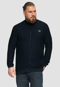 Dunkelblaues Zip-Jacket mit hohem Kragen, gerippten Manschetten und Saum, ausgestattet mit einem kleinen quadratischen Logo auf der linken Brust. Strukturierter Stoff.