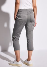 Pantalons gris crop avec une texture lisse, dotés de poches arrière et d'un design ajusté, associés à des baskets blanches sur un fond clair.