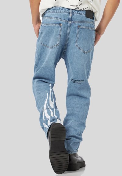 Jeans in denim azzurro chiaro con una vestibilità rilassata, caratterizzati da grafiche di fiamme bianche sulla gamba sinistra e dettagli del logo neri vicino alla vita.