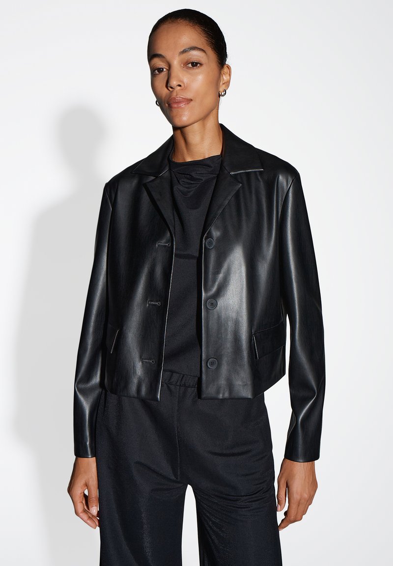 Zwarte cropped leren jas met een klassieke kraag, drie knopen en twee voorzakken, gecombineerd met een bijpassend zwart topje en broek.