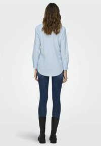 Light blue long-sleeve shirt with white stripes, paired with dark blue leggings and black knee-high boots. Casual fit with rounded hem.