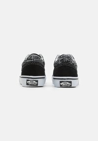 Zapatillas de ante negro con suela de goma blanca, con un upper de tela gris con patrón y un logo distintivo en el talón y la lengua.