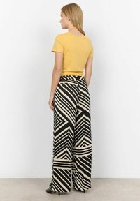 Yellow short-sleeve top paired with high-waisted black and beige striped wide-leg pants. Smooth fabric, geometric pattern, elastic waistband.