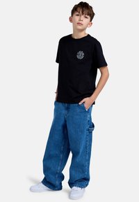 Černé bavlněné tričko s kruhovou grafikou na hrudi, spárované se světle modrými oversized džíny a bílými teniskami.