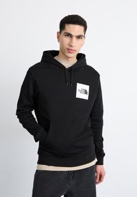 Felpa con cappuccio nera in cotone misto, con tasca a marsupio frontale e una toppa con logo bianco sul petto. Vestibilità casual.