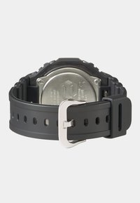 Bracelet de montre en caoutchouc noir avec perforations, boucle en métal et fond de boîtier en métal argenté avec détails en relief.