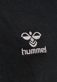 Svart textil med en grå broderad logotyp av en bi och ordet "hummel" under, med en slät, texturerad yta.