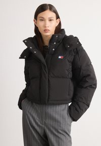 Casaco puffer preto com um design cropped, feito de material acolchoado, apresentando um colarinho alto, fecho de correr e um patch com logo no peito.