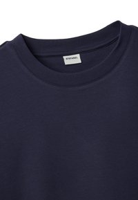 Detalle del tejido y cuello de camiseta de cuello redondo azul marino con una etiqueta de marca blanca "STEFANEL" cosida en el interior del cuello.