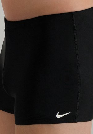 Schwarze Sportshorts aus dehnbarem Stoff, mit einem kontrastierenden weißen Logo auf der unteren rechten Seite und einer glatten Textur.