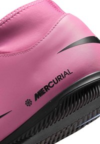 Nærbillede af en pink Nike Mercurial fodboldsko med sort sål, sort swoosh-logo og struktureret syning på den øverste del.
