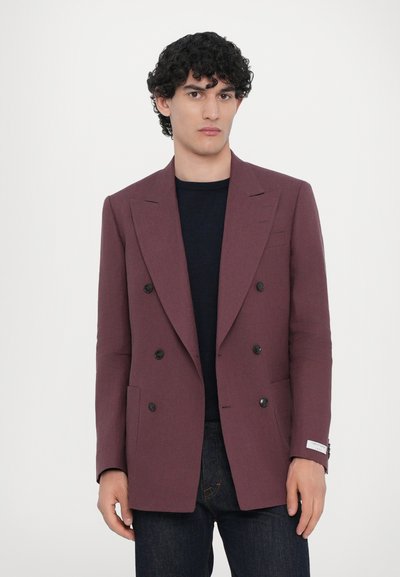 Doppelt angezogene Blazer aus tief burgunderfarbenem Stoff, mit schwarzen Knöpfen, Reverskragen und Seitentaschen. Getragen über einem marineblauen Oberteil mit dunkler Jeans.