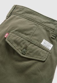 Olive green denim shorts with a back pocket, featuring a button closure and a Levi's label with white text. Subtle texture and stitching details.