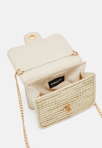 Beige crossbody bag with gold chain strap. The front features textured fabric with a woven pattern. Gold hardware clasp and branded tag visible inside.