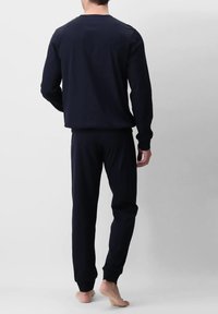 Maglietta a maniche lunghe blu scuro e pantaloni abbinati in tessuto soffice. Polsini e vita elasticizzati. A piedi nudi, vista da dietro su uno sfondo chiaro.