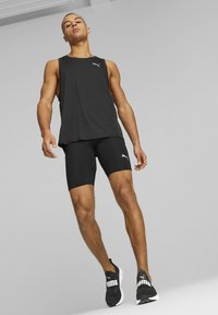 Camiseta sin mangas deportiva negra y pantalones cortos ajustados de tejido ligero, combinados con zapatillas deportivas negras con marca blanca.