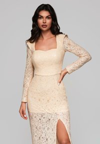 Blommönstrad klänning i ljusbeige med långa genomskinliga ärmar, fyrkantig halsringning, åtsittande överdel och sidofåra.