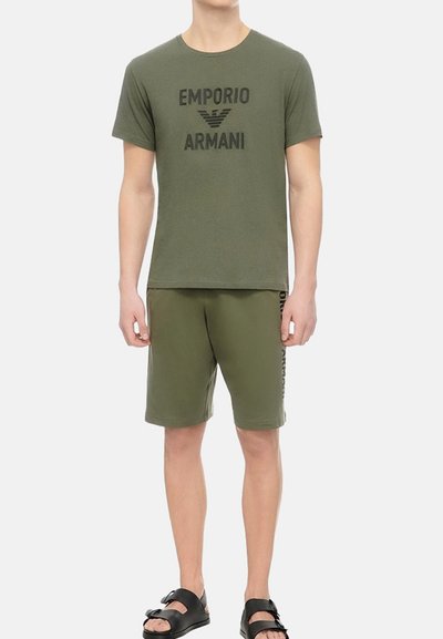 T-shirt en coton vert olive avec un logo "Emporio Armani" noir, associé à un short assorti et des sandales à glissière noires. Look décontracté de sport.