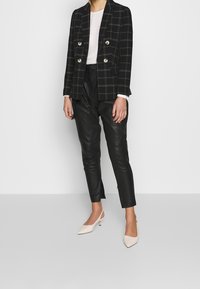 Svart rutig dubbelknäppt blazer med silverknappar, kombinerad med svarta avsmalnande skinnbyxor och beiga spetsiga klackar.