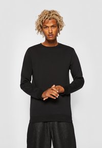 Zwarte sweatshirt met een ronde hals, lange mouwen en ribgebreide manchetten. Glad textuur met een relaxte fit, gecombineerd met donkere, gestructureerde broeken.