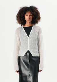 Lys grå, fluffy cardigan med lange ermer, v-hals, knappestolpe og en myk tekstur. Kombinert med et tettsittende svart skinnskjørt.