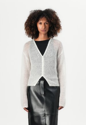 Lys grå, fluffy cardigan med lange ermer, v-hals, knappestolpe og en myk tekstur. Kombinert med et tettsittende svart skinnskjørt.