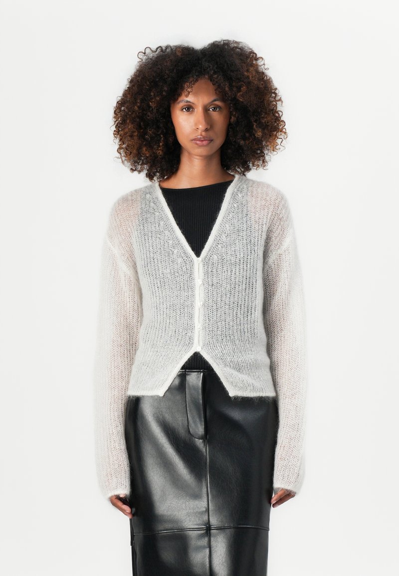 Lys grå, fluffy cardigan med lange ermer, v-hals, knappestolpe og en myk tekstur. Kombinert med et tettsittende svart skinnskjørt.