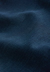 Țesătură de denim albastru închis cu o textură netedă, având un model subtil de țesătură în diagonală și o ușoară strălucire, evidențiind pliuri și cute.