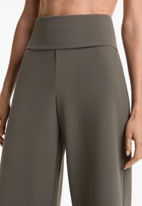 Weite, gerippte Hosen in einem sanften Olivgrün. Mit einem hohen, dehnbaren Bund und einer glatten Textur mit vertikalem Rippmuster.