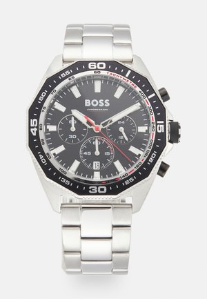 Montre chronographe en acier inoxydable argenté avec un cadran noir, des index blancs, des accents rouges et une échelle tachymétrique. Dispose d'un bracelet à maillons.