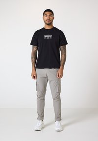 Camiseta de algodón negra con un diseño gráfico blanco, combinada con pantalones cargo gris claro con bolsillos laterales y zapatillas blancas.