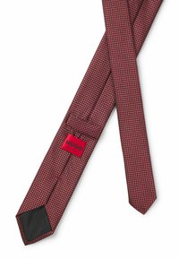 Rote Krawatte mit strukturiertem Muster und schlankem Design. Verfügt über ein schwarzes Ende und ein rotes Etikett mit "HUGO" in fetter Schrift. Hergestellt in Italien.