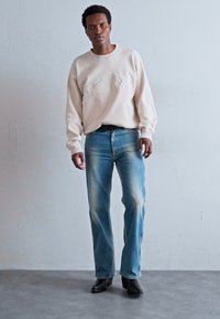 Beige sweatshirt with textured logo, paired with light blue, faded denim jeans. Black ankle boots with a pointed toe complete the look.