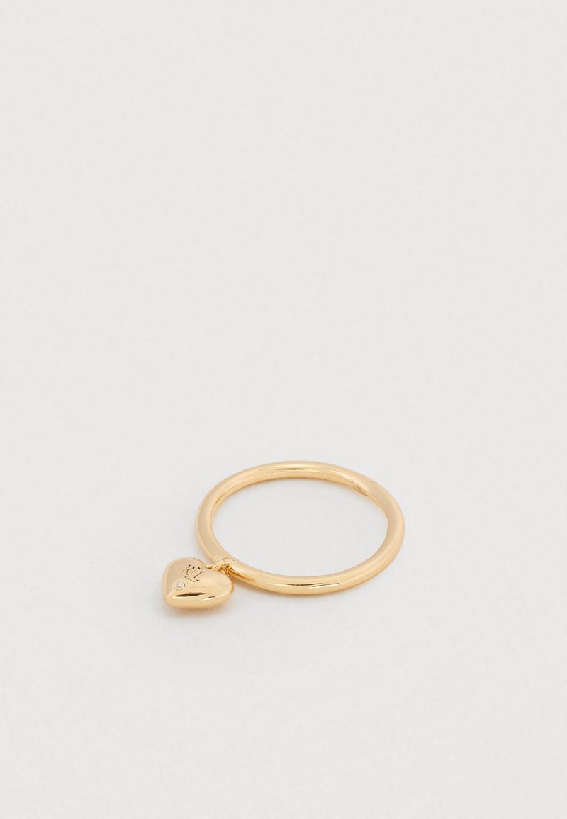 Kuldne sõrmus väikese südamekujuga ripatsiga, millele on graveeritud initsiaalid ja mis sisaldab väikest kivikest, valgel pinnal.