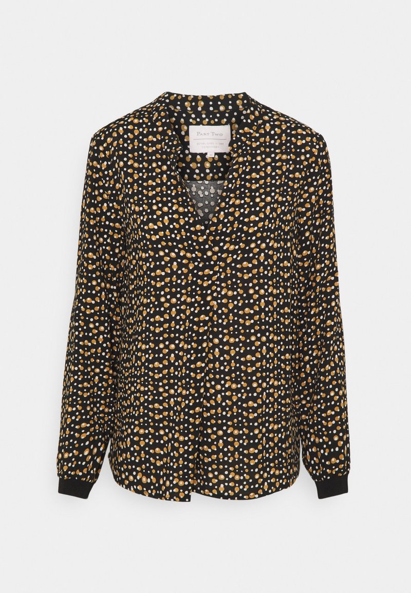 Blouse noire à manches longues avec des pois irréguliers orange et blancs et un col, présentée sur un fond uni.