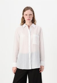Bílá košile na knoflíky s kapsou, nabízející zmačkanou texturu a jemný gradient, který přechází do světle šedé barvy na lemu. Součástí jsou dlouhé rukávy.