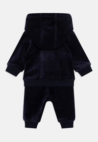 Ensemble de sport en velours bleu marine avec capuche, présentant des poignets et une taille côtelés, une texture lisse et un design simple.
