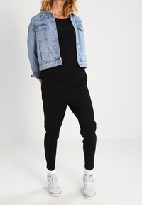 Jasnoniebieska kurtka jeansowa na czarnym topie, zestawiona z czarnymi zwężanymi spodniami i białymi tenisówkami. Prosty design, luźny krój i minimalne detale.