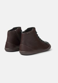 Stivaletti in pelle marrone con lacci verdi, chiusura con zip sul retro e punta arrotondata. Texture morbida con una suola in gomma flessibile.